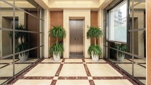 A modern hallway with a checkered floor, a central elevator, and potted plants on either side. - Xi Ge Hotel (Chengdu)