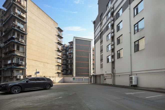 Un edificio residencial de varios pisos con balcones, una zona de estacionamiento y cielo despejado.