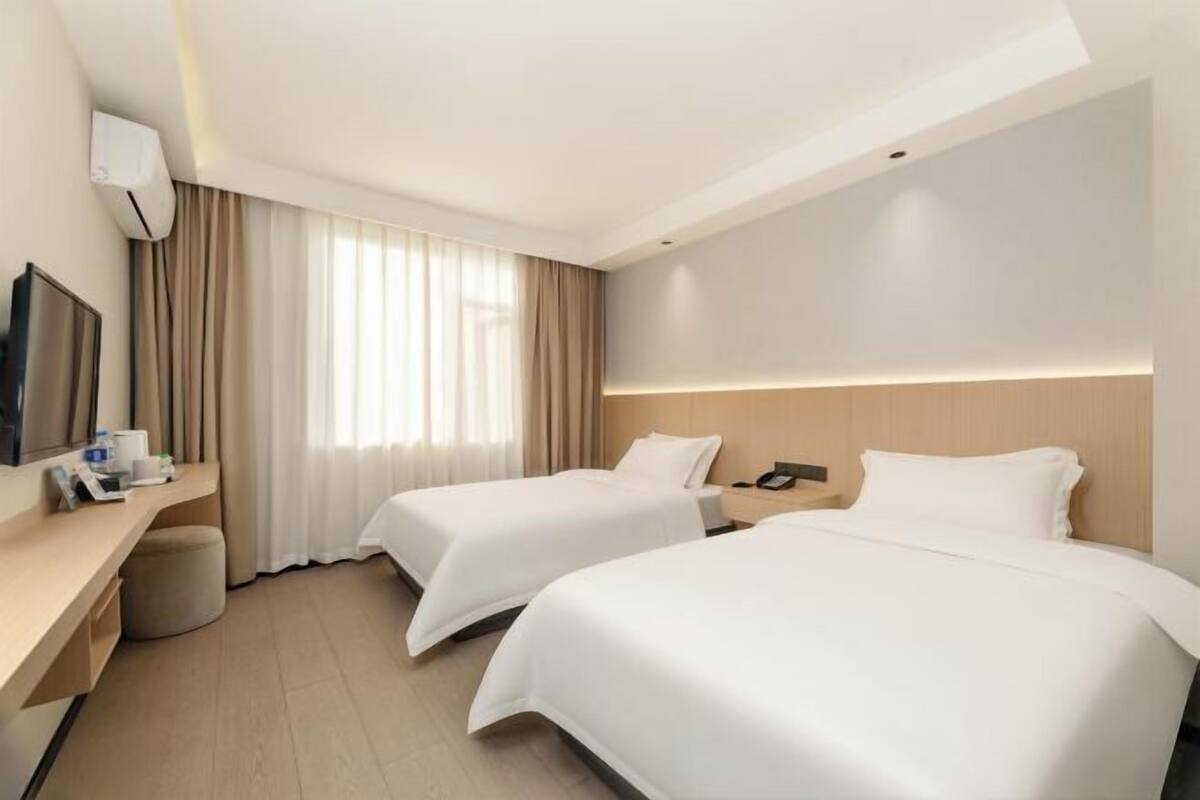 A hotel room with two beds, a desk, a TV, and a window with curtains.