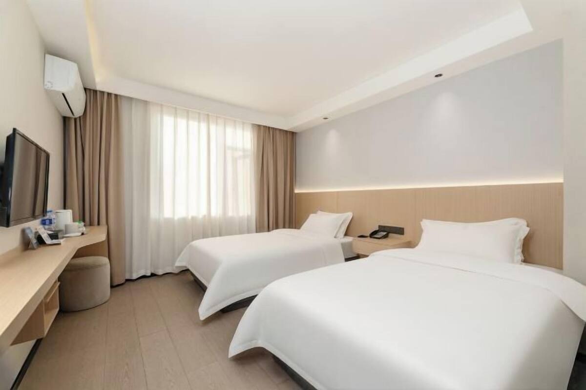 A hotel room with two beds, a desk, a TV, and a window with curtains.