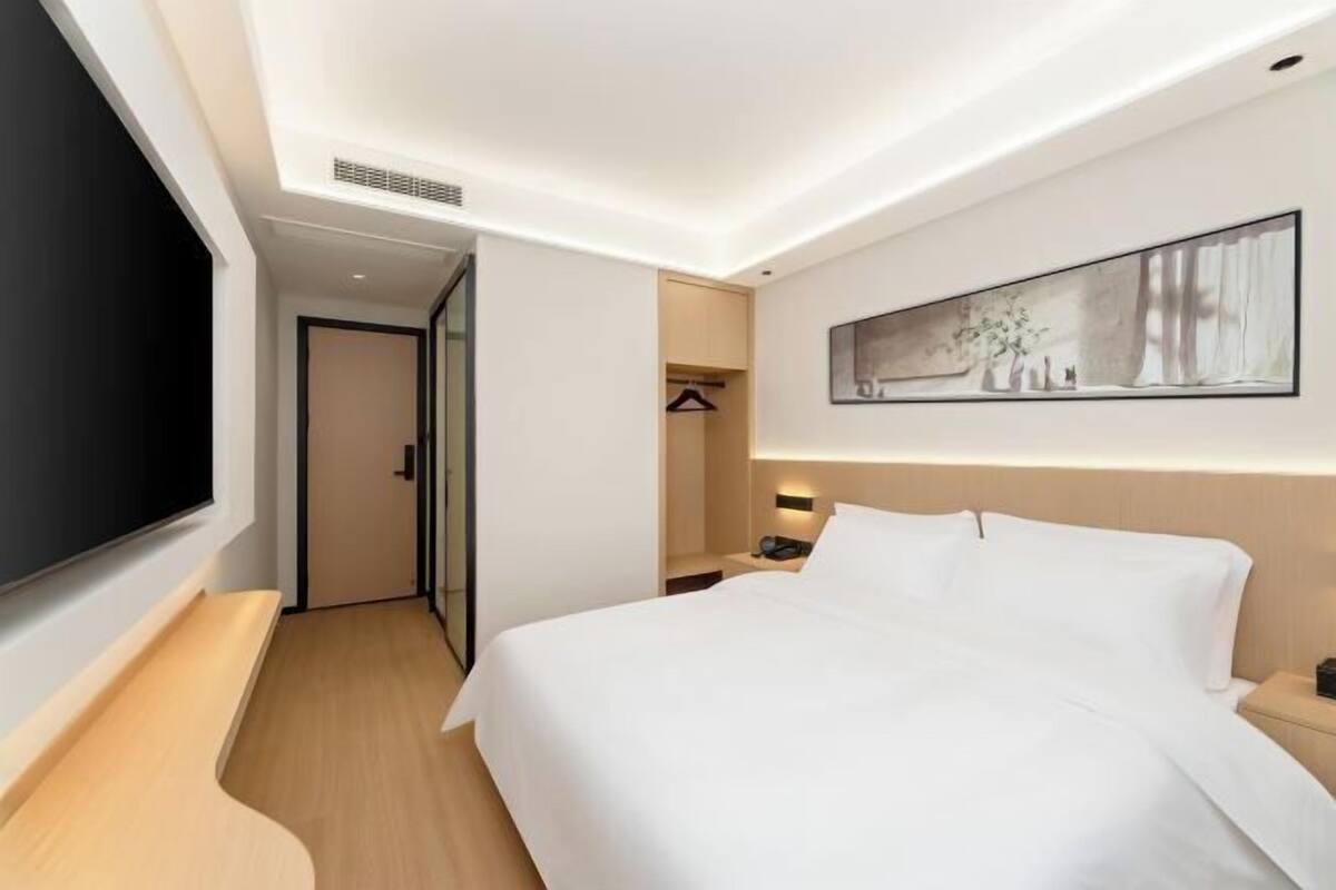 A modern hotel room with a large bed, a flat-screen TV, a painting on the wall, and a walk-in closet.
