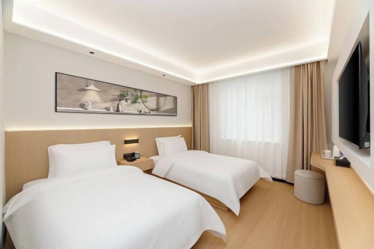 A hotel room with two beds, a flat-screen TV, a painting on the wall, and a window with curtains.