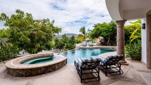Una piscina con sillones de descanso, rodeada de exuberante vegetación y vistas a montañas distantes.