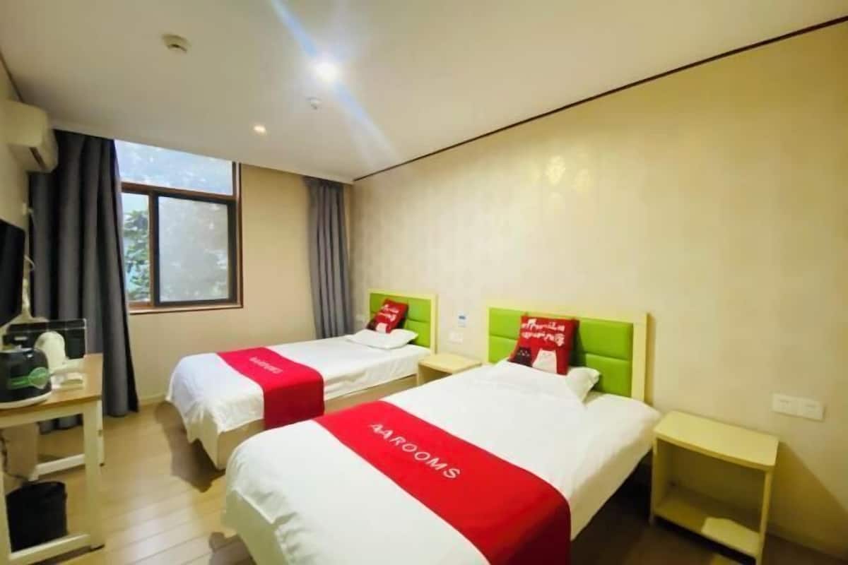 Habitación de hotel con dos camas, cada una con cubrecama rojo y blanco, cabecero verde y mesita de noche pequeña.