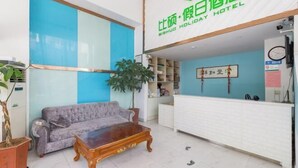 Un espace d’accueil d’hôtel comprenant un canapé, une table basse en bois, un comptoir de réception et une grande plante.