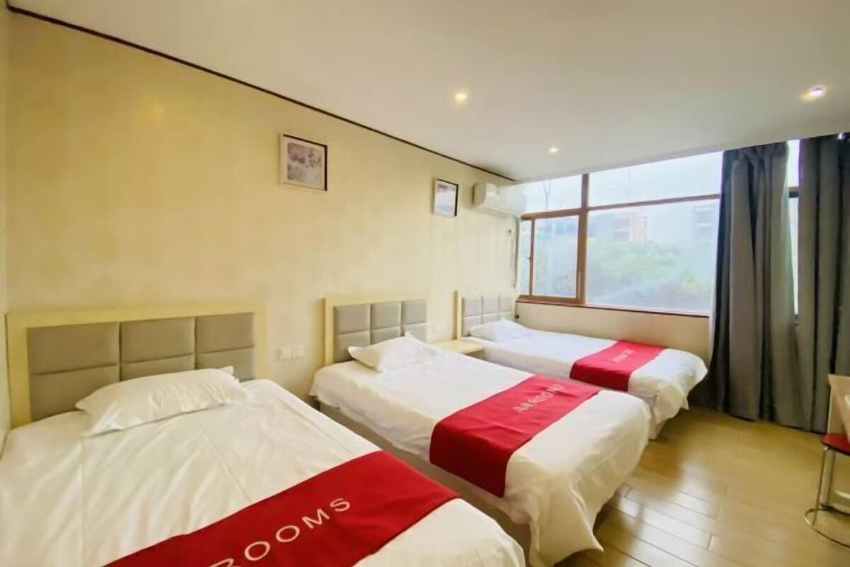 Habitación de hotel con tres camas, cada una con cubrecama rojo y blanco, y un ventanal con cortinas.