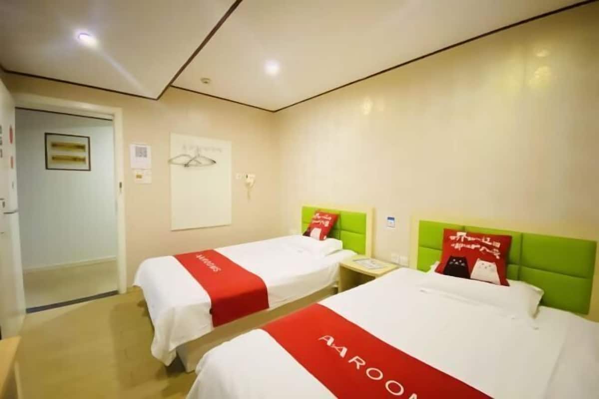 Habitación de hotel con dos camas, cada una con una colcha rojo y blanco, cabecero verde y una mesita de noche con lámpara.