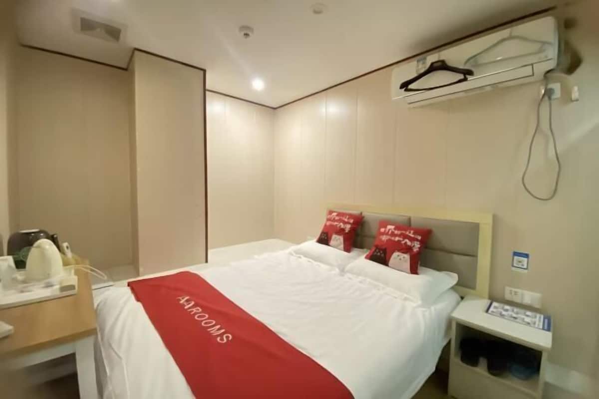 Una habitación de hotel con una cama, una mesita de noche, un perchero y un equipo de aire acondicionado de pared.