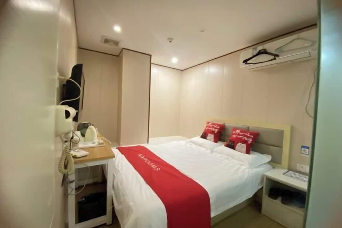 Una habitación de hotel con cama, mesita de noche con teléfono, pequeño armario y aire acondicionado instalado en la pared.