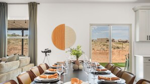 Un comedor con una mesa larga dispuesta para una comida, una cámara sobre un trípode y una vista al desierto a través de amplios ventanales.
