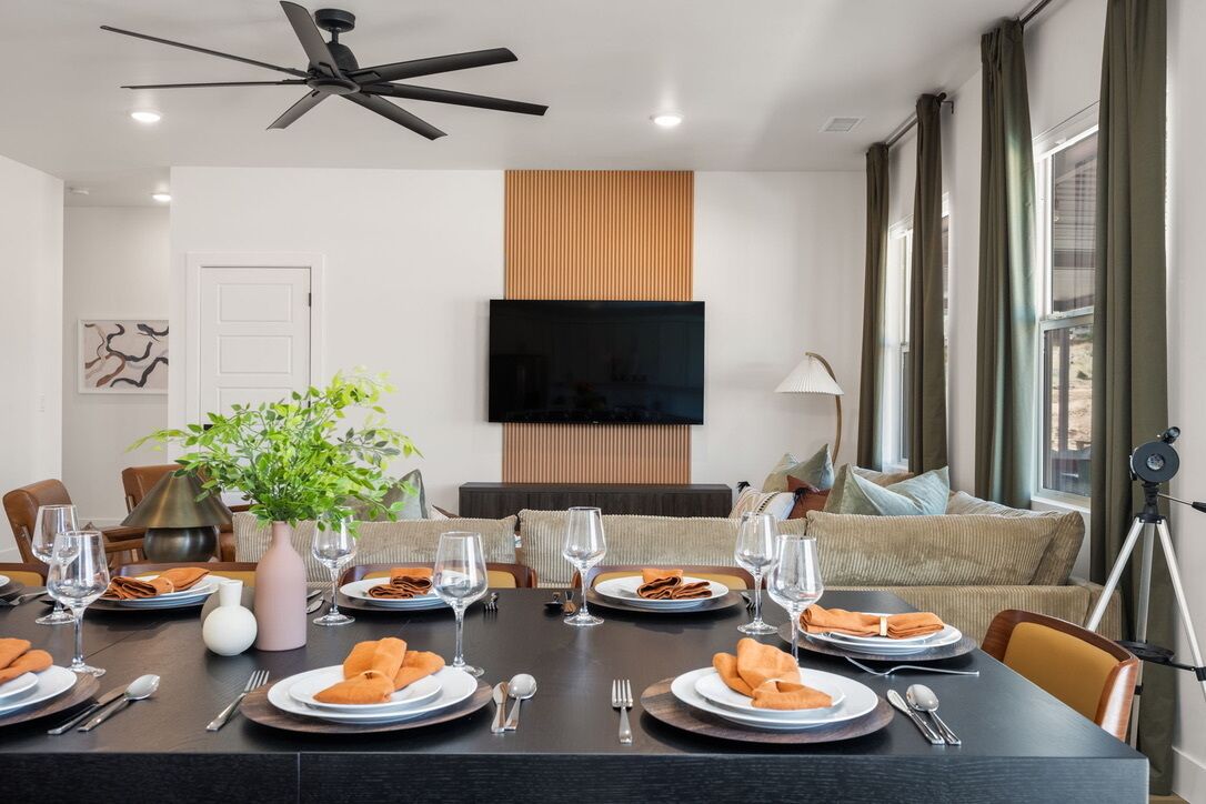 Un coin repas avec une table dressée pour quatre personnes, un ventilateur de plafond, un téléviseur à écran plat et un trépied placé à droite.