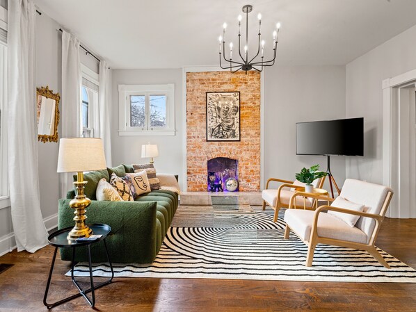 Ein Wohnzimmer mit einem grünen Sofa, einem gemusterten Teppich, einem Kamin und einem Fernseher.