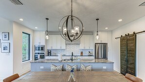 A modern kitchen with white cabinets, a large island, and a wooden dining table with chairs. - NEW LISTING! Stunning Lakehouse with Views, Hot Tub & Game Room! (Lago Vista)
