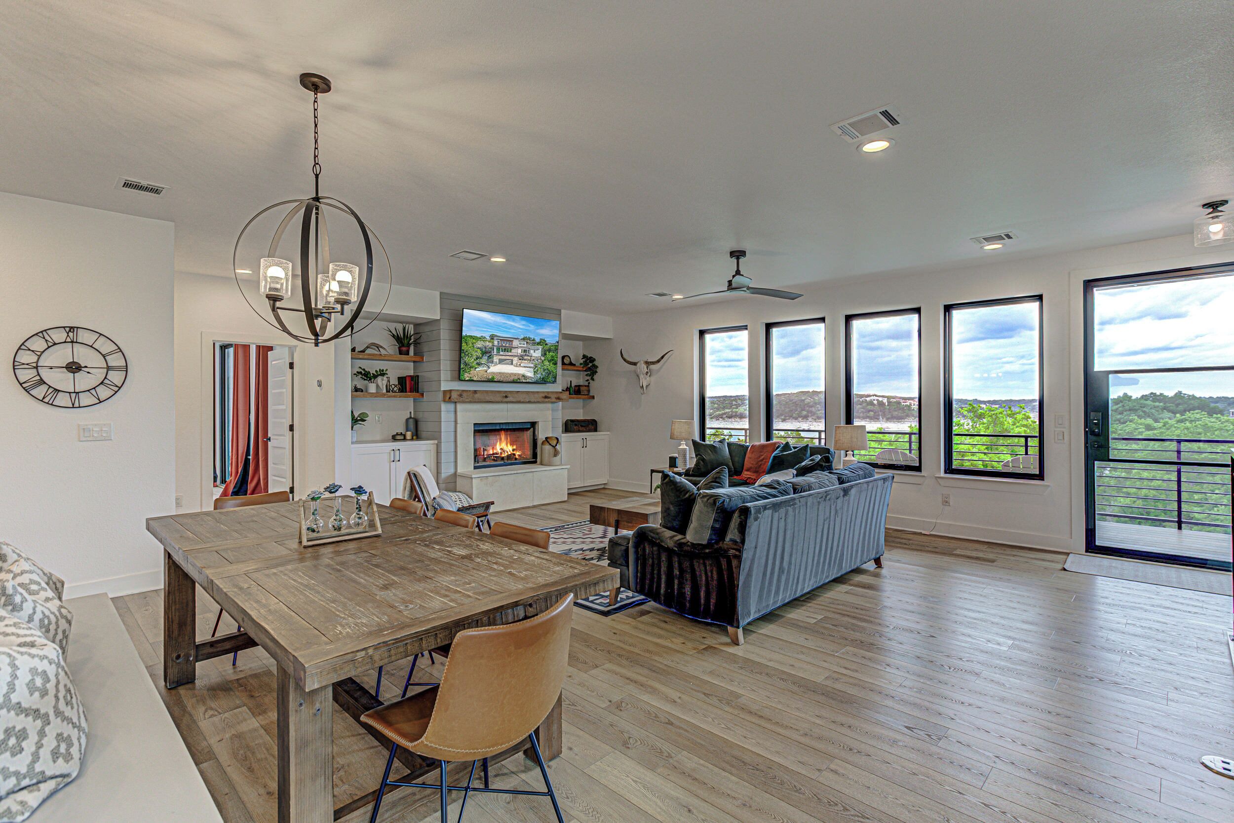 A spacious living area with a wooden dining table, comfortable seating, a fireplace, and large windows offering a view of the outdoors.