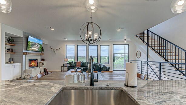A spacious living area with a large marble countertop, a fireplace, a television, and a staircase. - NEW LISTING! Stunning Lakehouse with Views, Hot Tub & Game Room! (Lago Vista)