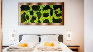 A neatly made double bed with two pillows and two rolled towels, a wall-mounted abstract art piece, and two bedside tables with wall-mounted lights. - BoRa Apartment Heaven (Villach)
