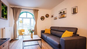 A modern living room with a grey sofa, yellow cushions, a wooden coffee table, and a view through a large window with curtains. - BoRa Apartment Heaven (Villach)