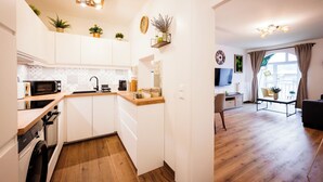 A compact kitchen with white cabinets, a microwave, and a sink. There are plants on the countertop and a dining area with a table and chairs. - BoRa Apartment Heaven (Villach)