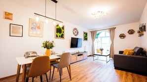 A modern living room with a dining area, wooden flooring, a flat-screen TV, and a sofa with cushions. - BoRa Apartment Heaven (Villach)