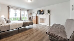 A modern bedroom with a bed, a sofa, a TV, and a fireplace. - Rainier Guesthouse - Walk to Metro (Seattle)