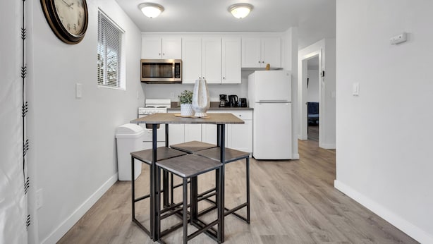 A modern kitchen with white cabinets, a microwave, a refrigerator, and a dining area with a table and chairs. - Rainier Guesthouse - Walk to Metro (Seattle)