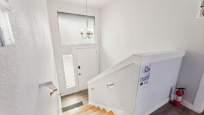 A clean, white interior with a wooden staircase, a door with frosted glass, and a fire extinguisher on the floor. - Rainier Guesthouse - Walk to Metro (Seattle)
