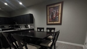 A dining area with a dark wooden table and chairs, a kitchen in the background, and a framed artwork on the wall. - Gates at Sour Lake #502 (Sour Lake)