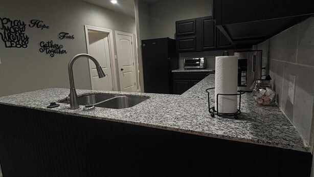A modern kitchen with a granite countertop, stainless steel sink, and black cabinets. - Gates at Sour Lake #502 (Sour Lake)