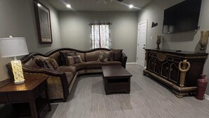 A living room with a sectional sofa, a coffee table, a TV mounted on the wall, and a ceiling fan. - Gates at Sour Lake #502 (Sour Lake)