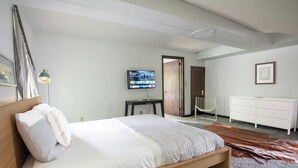 A bedroom with a wooden bed, a television on the wall, a white dresser, and a leather rug.