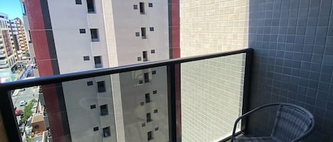 Un balcon avec deux fauteuils en osier et une table en verre, offrant une vue sur un paysage urbain dominé par de hauts immeubles.