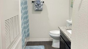 Een compacte badkamer met toilet, een handdoekrek met een decoratieve handdoek, een douchegordijn en een kleedje op de vloer.