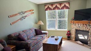 A living room with a sofa, a coffee table, a fireplace, and a TV. - 2 bed/2 bath ground level condo, right on hike & bike trails, fireplace (Silver Star Mountain)