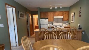 A dining area with a wooden table and chairs, a kitchen with wooden cabinets, and a door leading to another room. - 2 bed/2 bath ground level condo, right on hike & bike trails, fireplace (Silver Star Mountain)