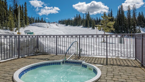 A hot tub with a view of a snowy mountain and a fenced area. - 2 bed/2 bath ground level condo, right on hike & bike trails, fireplace (Silver Star Mountain)
