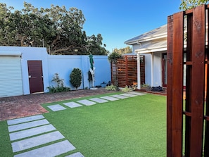 A residential backyard with artificial grass, a brick pathway, a wooden fence, and a garage.