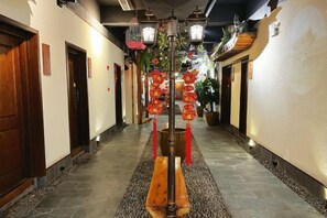 A corridor with a wooden bench, red lanterns, and a hanging light fixture.