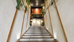 Un escalier avec des rampes en bois et un revêtement de sol en moquette, menant à une pièce dotée d’une porte en bois et d’une enseigne rouge au-dessus.