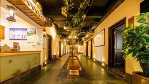 Un hall d’hôtel avec un sol en pierre, un comptoir d’accueil et une plante sur la droite.