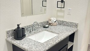 Een badkamer met een wastafel met een granieten blad, een spiegel, een zwart kastje en een toilet.