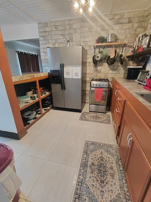 A kitchen with a refrigerator, stove, microwave, and various utensils on the wall. - The Suncrest Private Suite. (BirdRock)