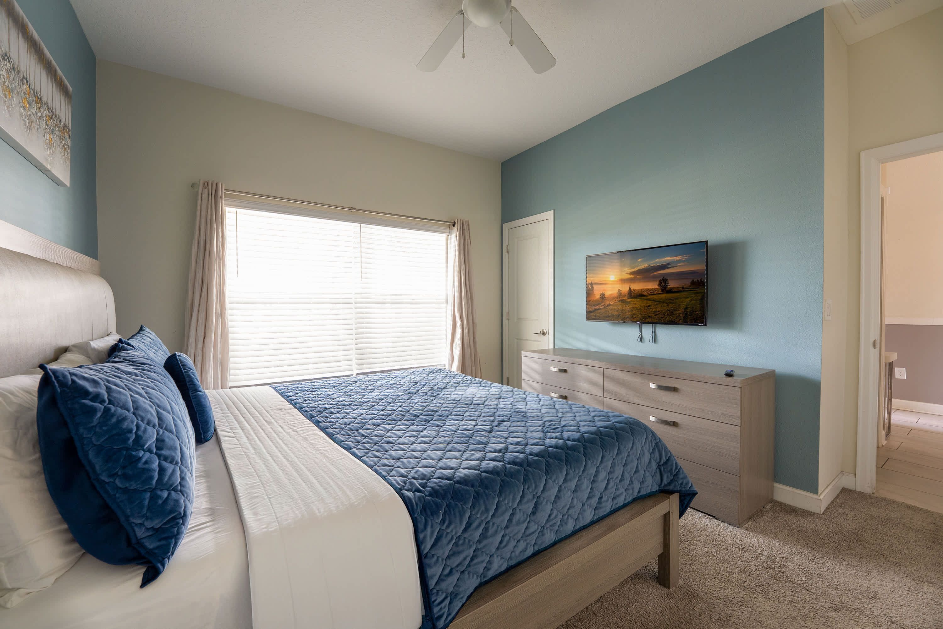 A bedroom with a bed, a dresser, a television, and a window with curtains.