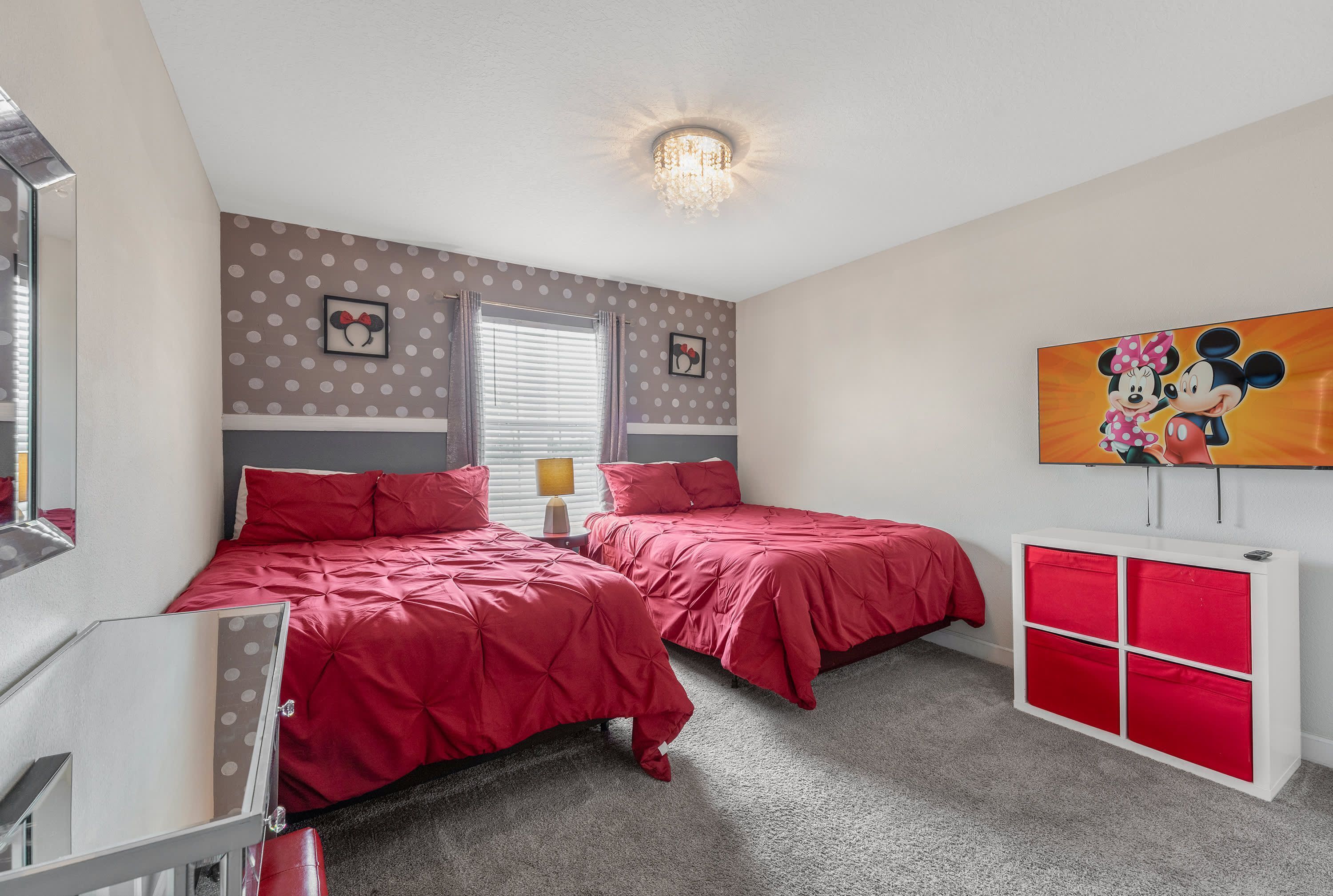 A bedroom with two beds, a vanity with a mirror, and a Mickey Mouse painting on the wall.