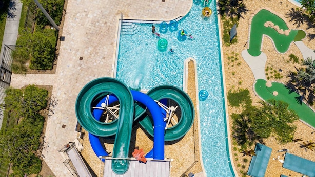An aerial view of a swimming pool area with a water slide, a small pool, and surrounding landscaping. - Relax Near Disney 4BR Home With Pool (Kissimmee)
