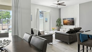 A modern living room with a dining area, a ceiling fan, and a TV mounted on the wall. - Relax Near Disney 4BR Home With Pool (Kissimmee)