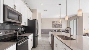 A modern kitchen with stainless steel appliances, a central island with a sink, and pendant lighting. - Relax Near Disney 4BR Home With Pool (Kissimmee)