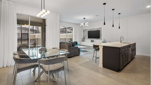 A modern kitchen with a central island, a dining area with a glass table, and a living space with a sofa and TV. - Stylish Family Retreat With Themed Bedrooms (Kissimmee)