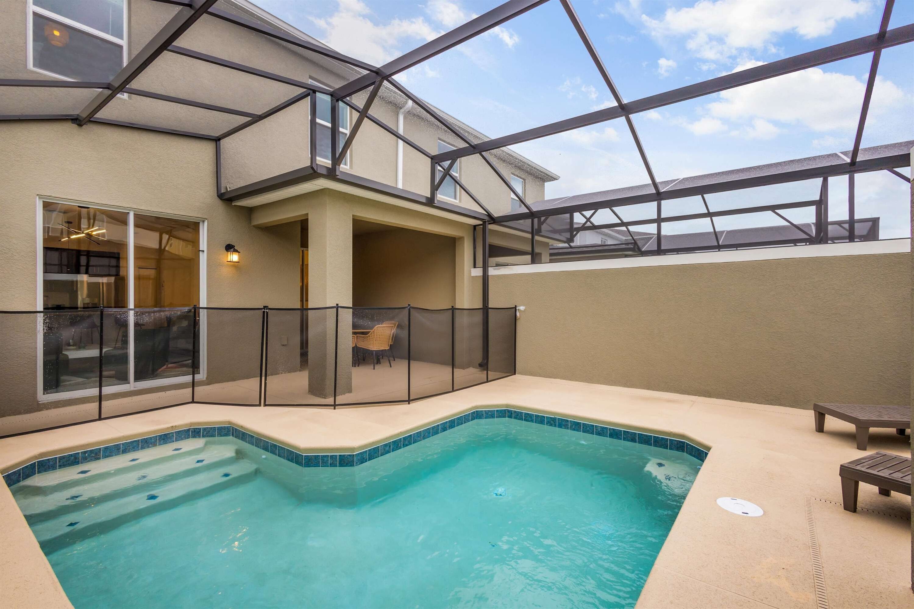 An indoor swimming pool with a glass enclosure, a covered seating area, and a view of the sky.
