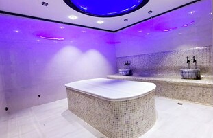 Een moderne badkamer met een vrijstaand bad, betegelde muren met mozaïek en een ronde plafondlamp.