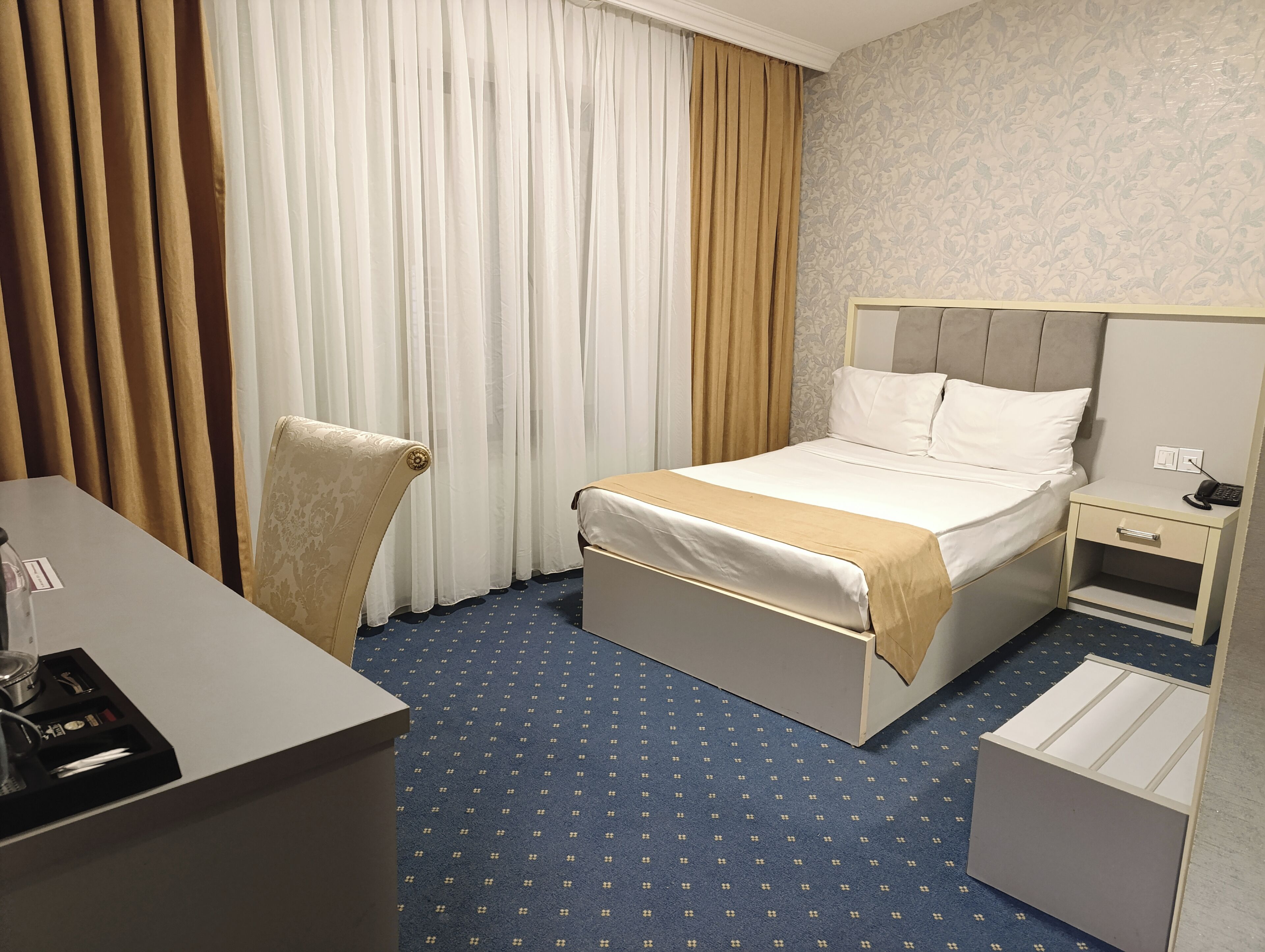 Ein Hotelzimmer mit Bett, Schreibtisch, Stuhl, Nachttisch und kleinem Tisch.
